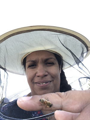 Woman wearing beekeeper hat and bee sitting on her index finger.