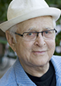 Headshot of Norman Lear, who is wearing a white hat, black shirt and light blue jacket