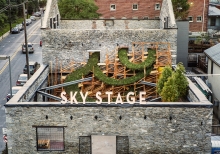 A photo from above of a gray stone building with an open rooftop area featuring trees and other plants and the words “Sky Stage” on the roof edge.