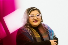 A smiling woman in cat-eye glasses and a colorful plaid scarf.