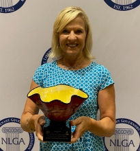 A smiling person with blond hair holding a red and yellow sculptural award
