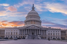 Neoclassical architecture of marble U.S. Capitol dome with bright blue sky at sunset and purple-orange clouds in background.