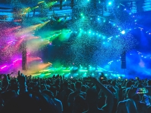 It's a photo of a large crowd at a concert, with rainbow colors lighting up the stage.