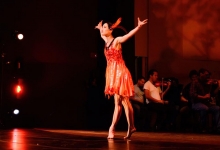 A dancer in a flowy orange dress strikes a pose on a stage.